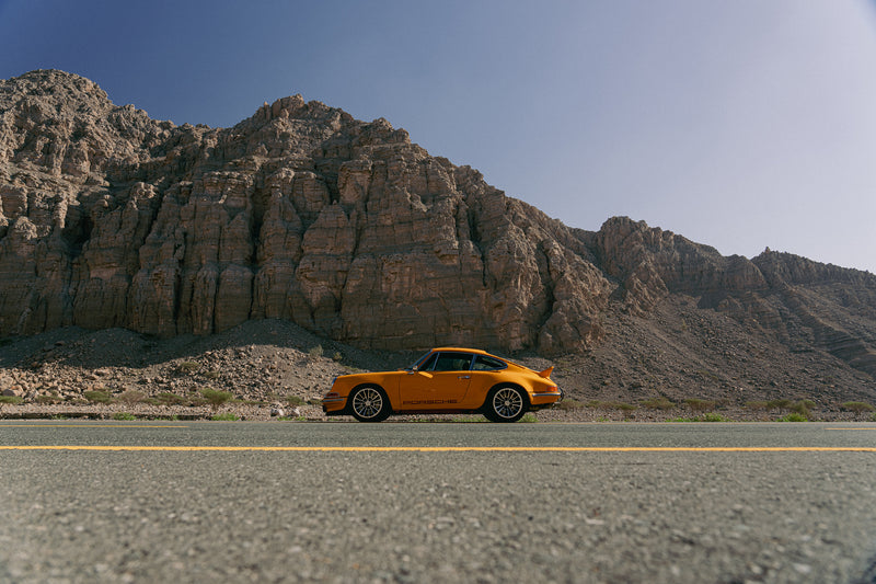 Yellow Triebwerk F4.3 Porsche 911 on a desert road with rocky mountains in the background
