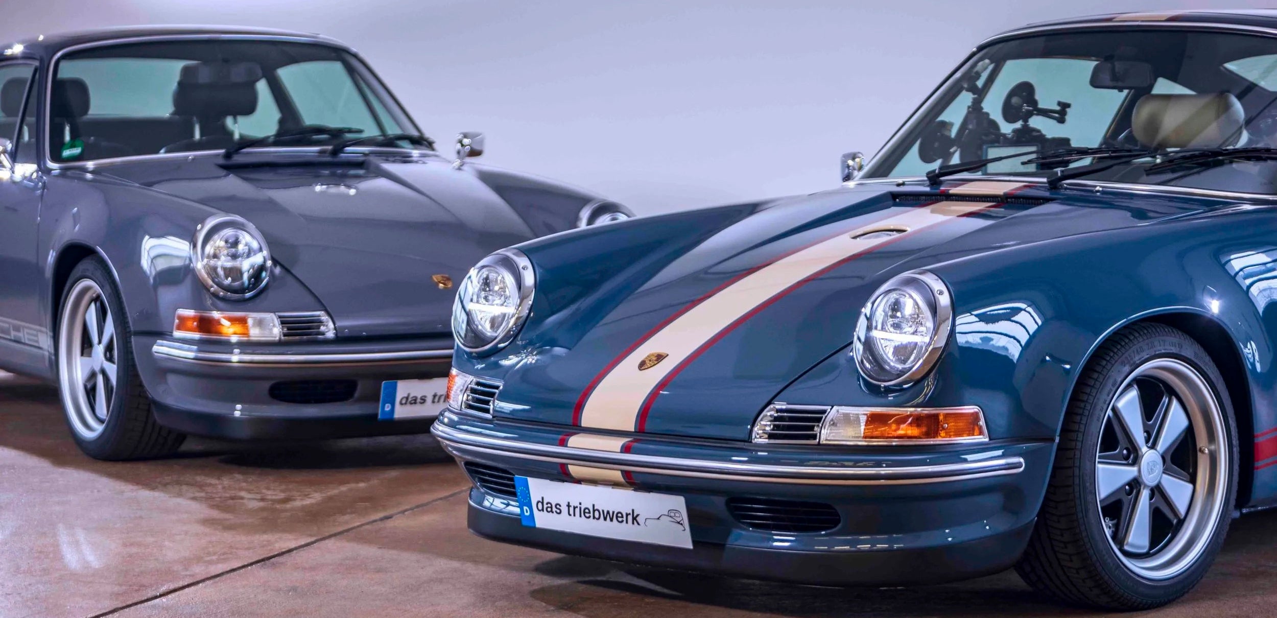 Two Triebwerk Porsche 911 parked side by side on a concrete surface.