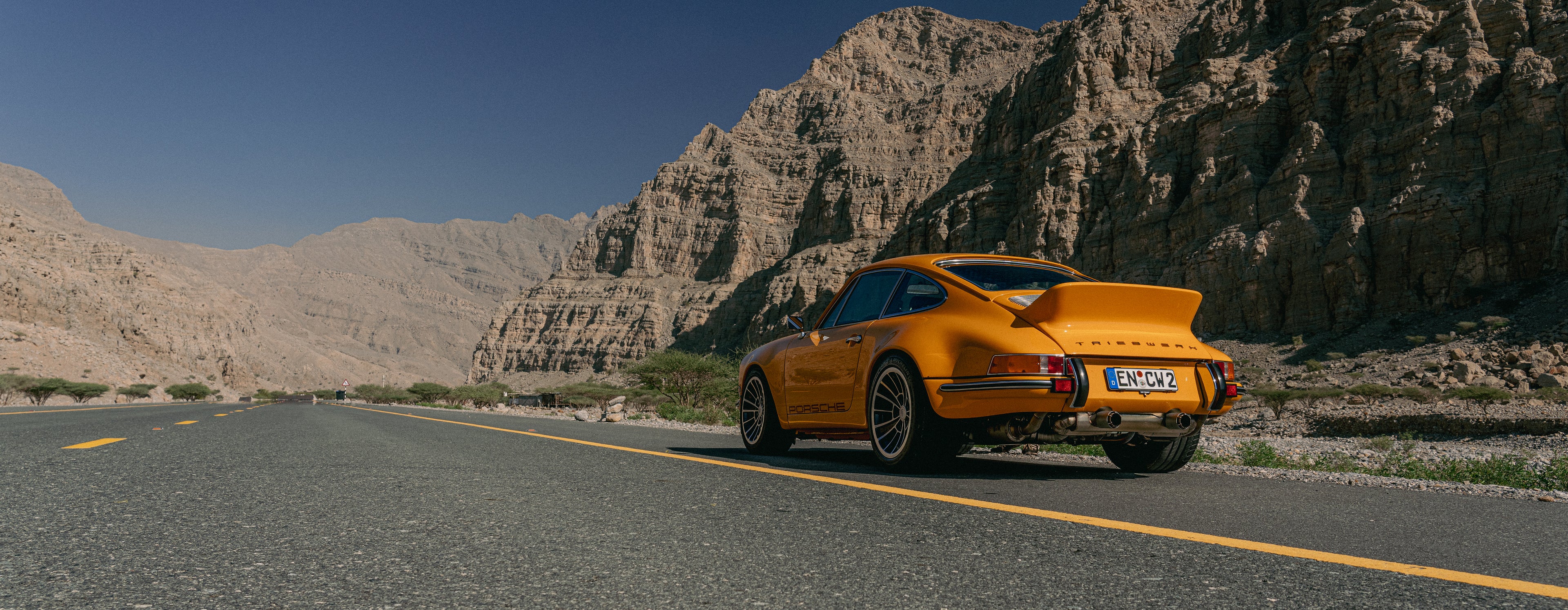 Yellow Triebwerk F4.3 Porsche 911 on a road with a rocky mountain background.