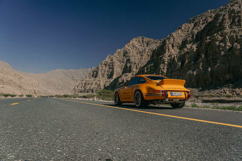 Yellow Triebwerk F4.3 Porsche 911 on a desert road with mountains in the background