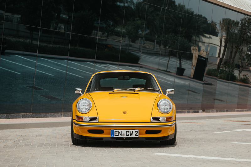 Yellow Triebwerk F4.3 Porsche 911 parked in front of a reflective building