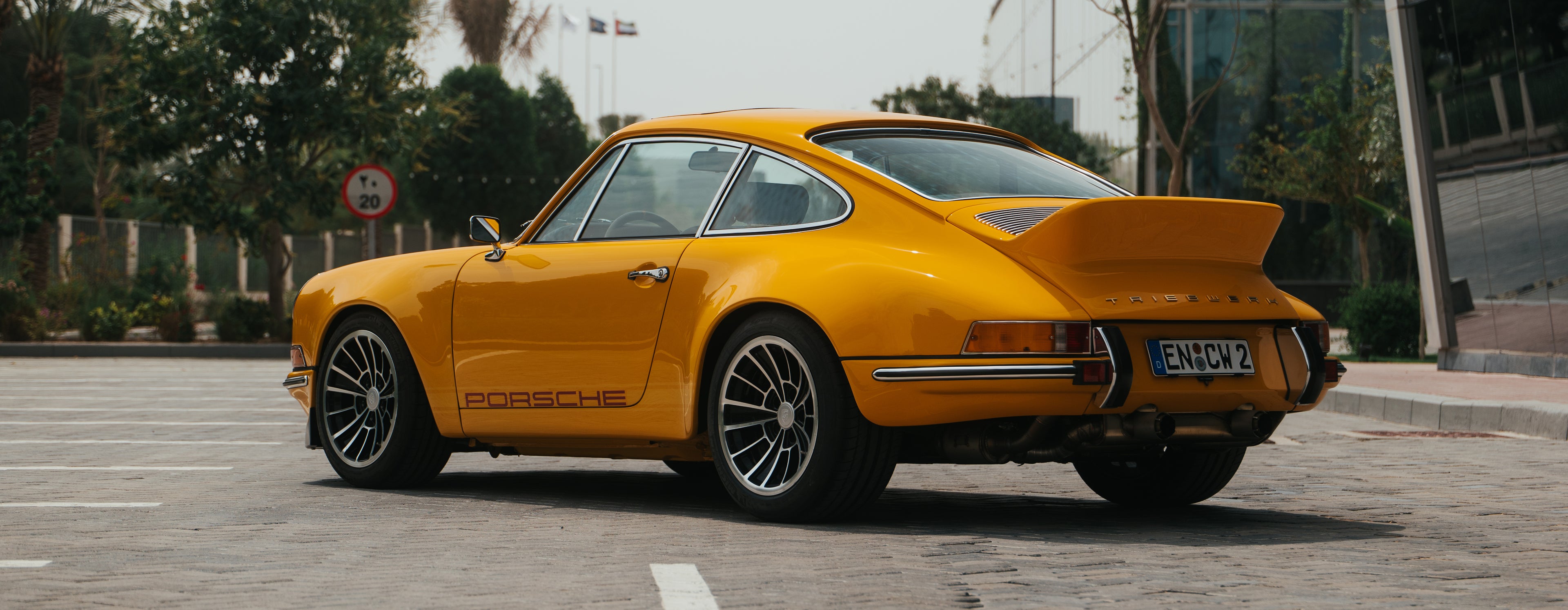 Yellow triebwerk f4.3 porsche 911 parked on a street with trees and buildings in the background