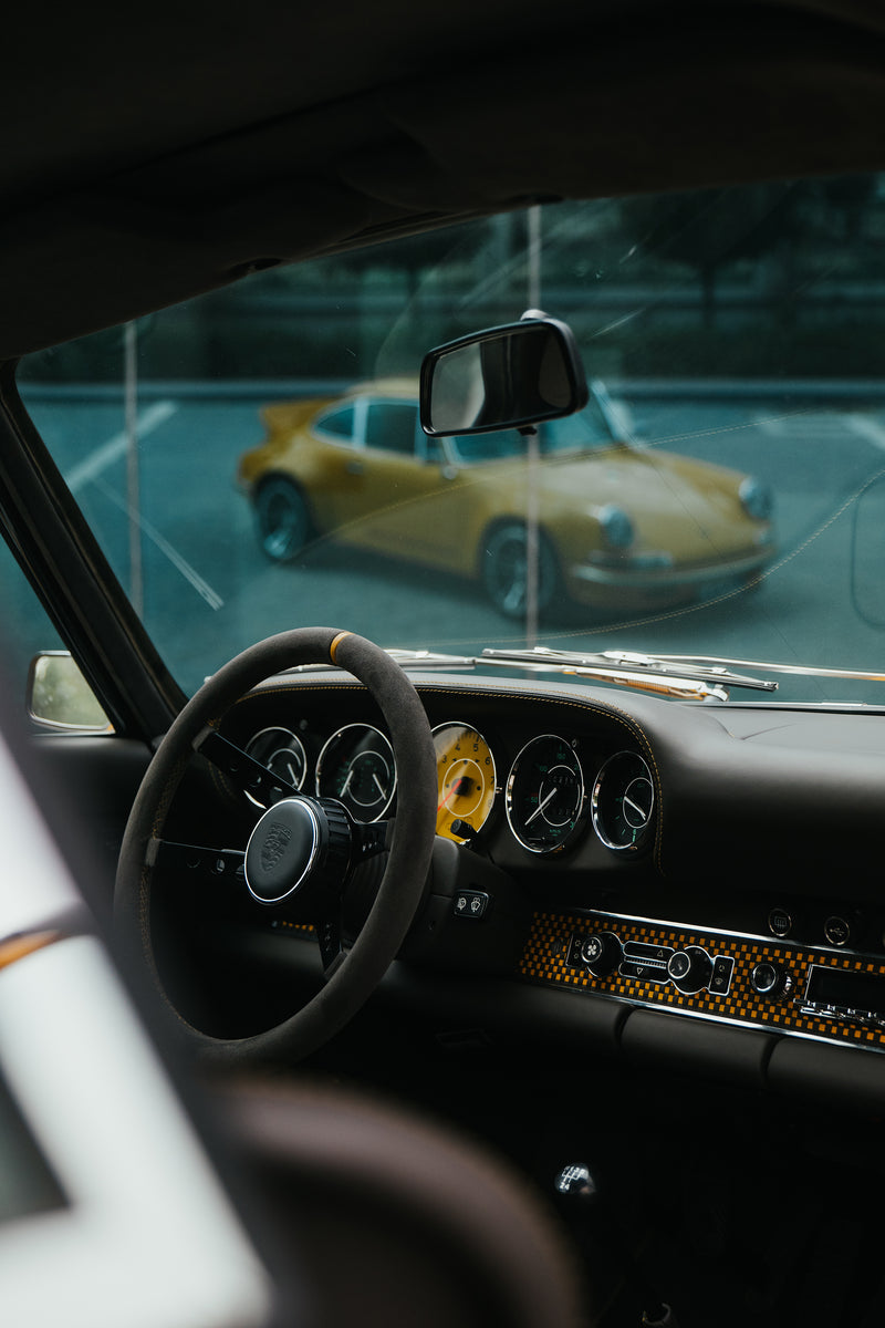 Yellow Triebwerk F4.3 Porsche 911  interior with dashboard and steering wheel, blurred reflection of the Yellow Triebwerk F4.3 Porsche 911 outside.
