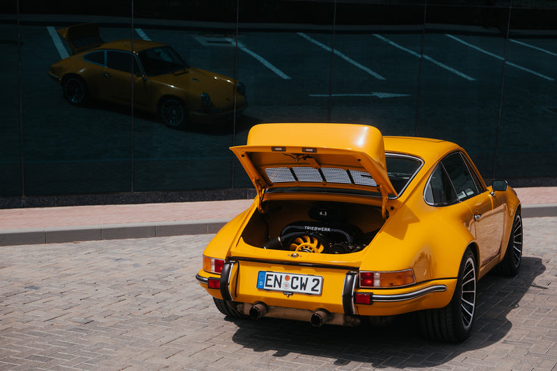 Yellow Triebwerk F4.3 Porsche 911 with open engine cover with reflection on building window in background.