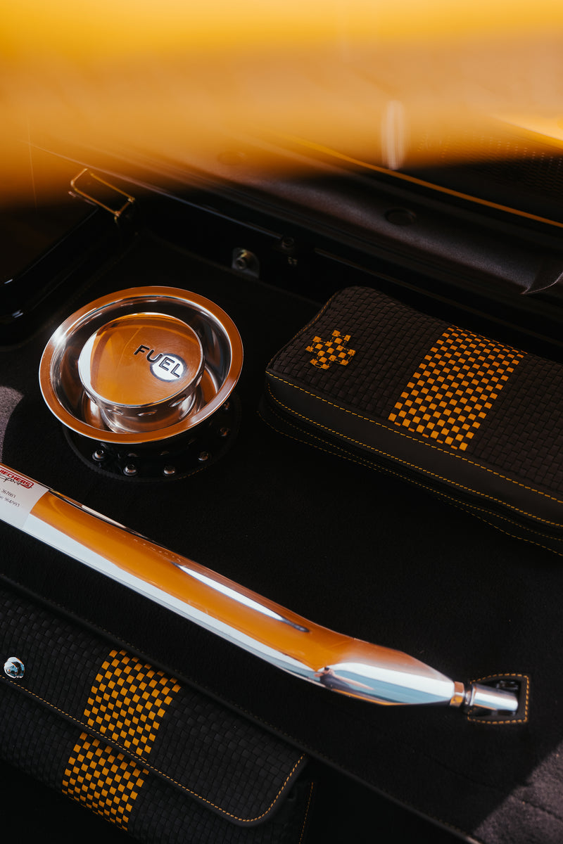 Close-up of a Yellow Triebwerk F4.3 Porsche 911 fuel cap and polished strut brace on a black interior background