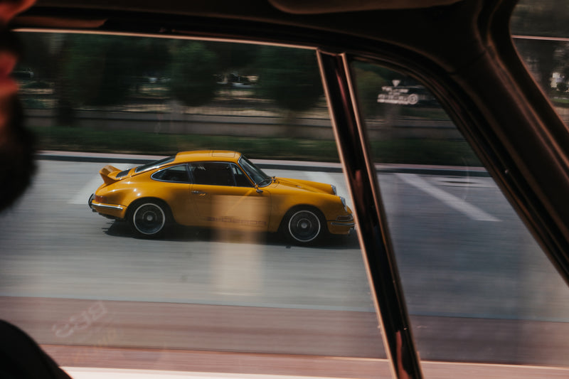 Reflection of Yellow Triebwerk F4.3 Porsche 911 on window driving.