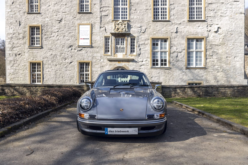 Gray Triebwerk F3.8 parked in front of a stone building with a garden.