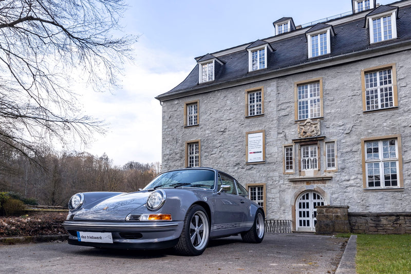Gray Triebwerk F3.8 parked in front of a large 4-story stone building with multiple windows.
