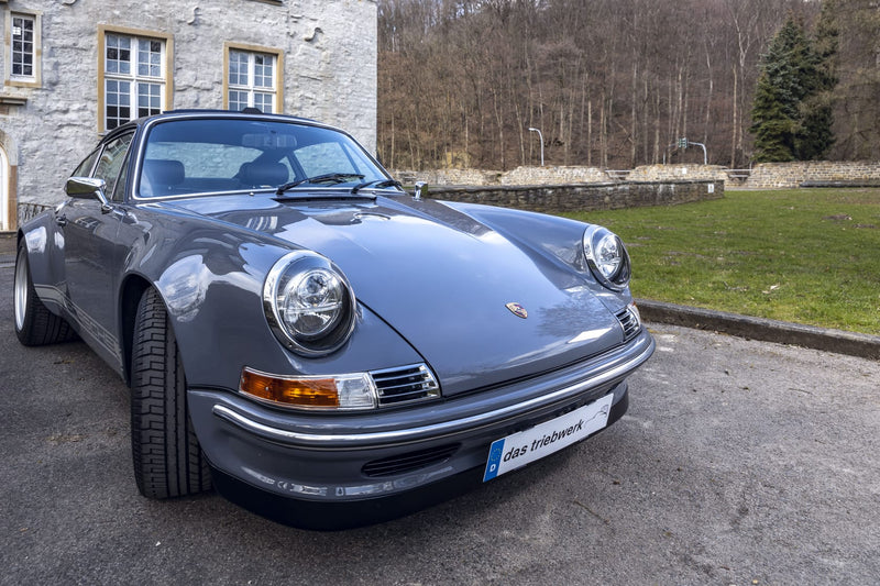 Gray Triebwerk F3.8 parked in front of a stone building with trees in the background
