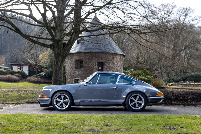 Side profile of Gray Triebwerk F3.8 parked in front of a stone building with trees in the background