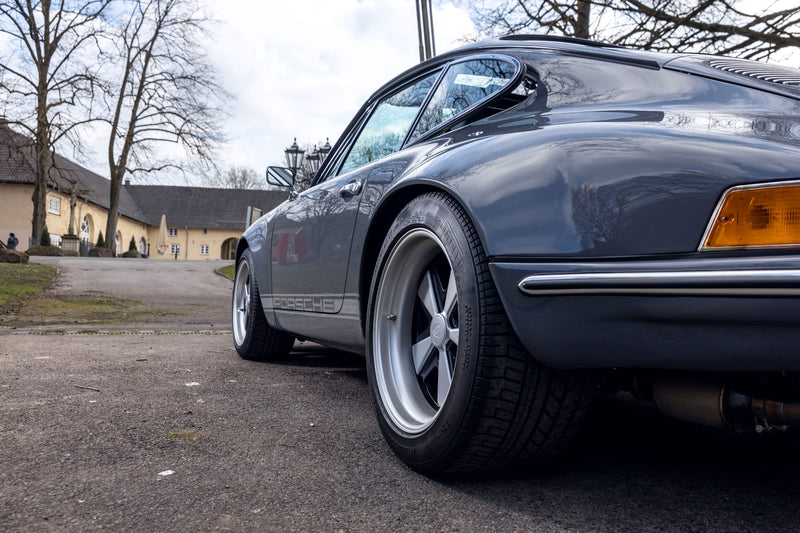 Close up of rear wheel and tire of a Gray Triebwerk F3.8 parked on a street with buildings in the background