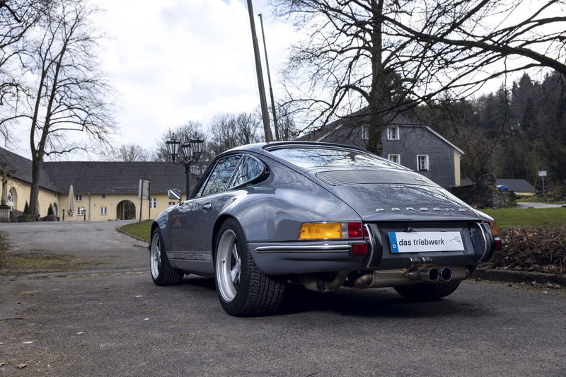 Gray Triebwerk F3.8 parked on a road with buildings and trees in the background