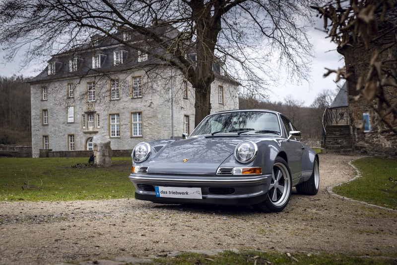 Gray Triebwerk F3.8 parked in front of a large building with trees and grass.