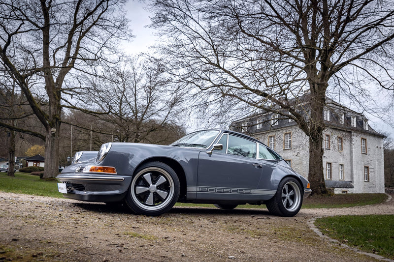 Gray Triebwerk F3.8 parked on a gravel driveway with trees and a building in the background