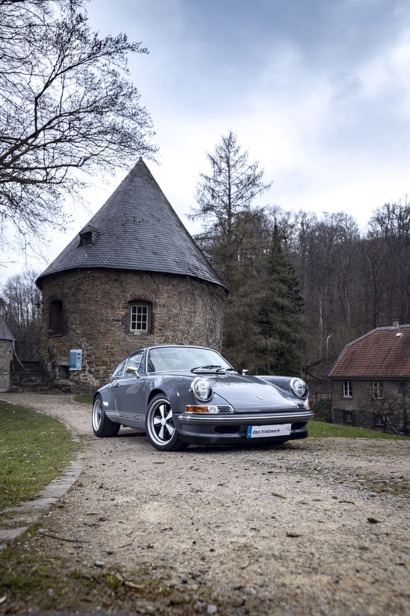 Gray Triebwerk F3.8 parked in front of a historic building with a tower.