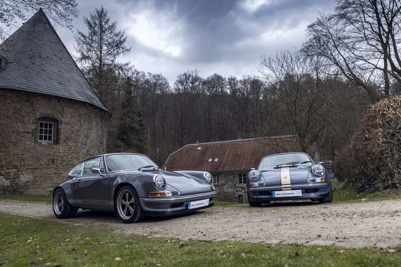 Gray Triebwerk F3.8 and Triebwerk F350 parked in front of a rustic building with trees in the background.