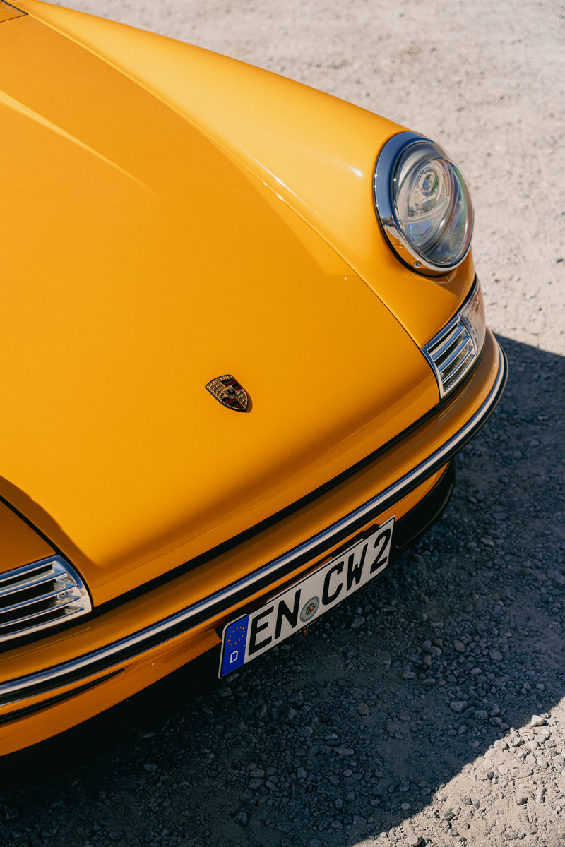Close-up of a Yellow Triebwerk F4.3 Porsche 911 with a visible license plate on a road.