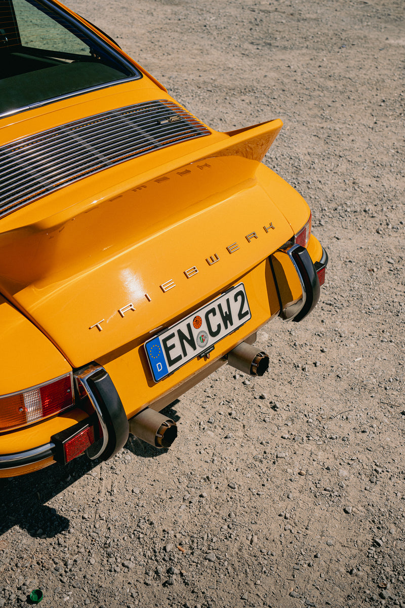 Rear of Yellow Triebwerk F4.3 Porsche 911  ducktail and custom exhaust tips on a dirt road.