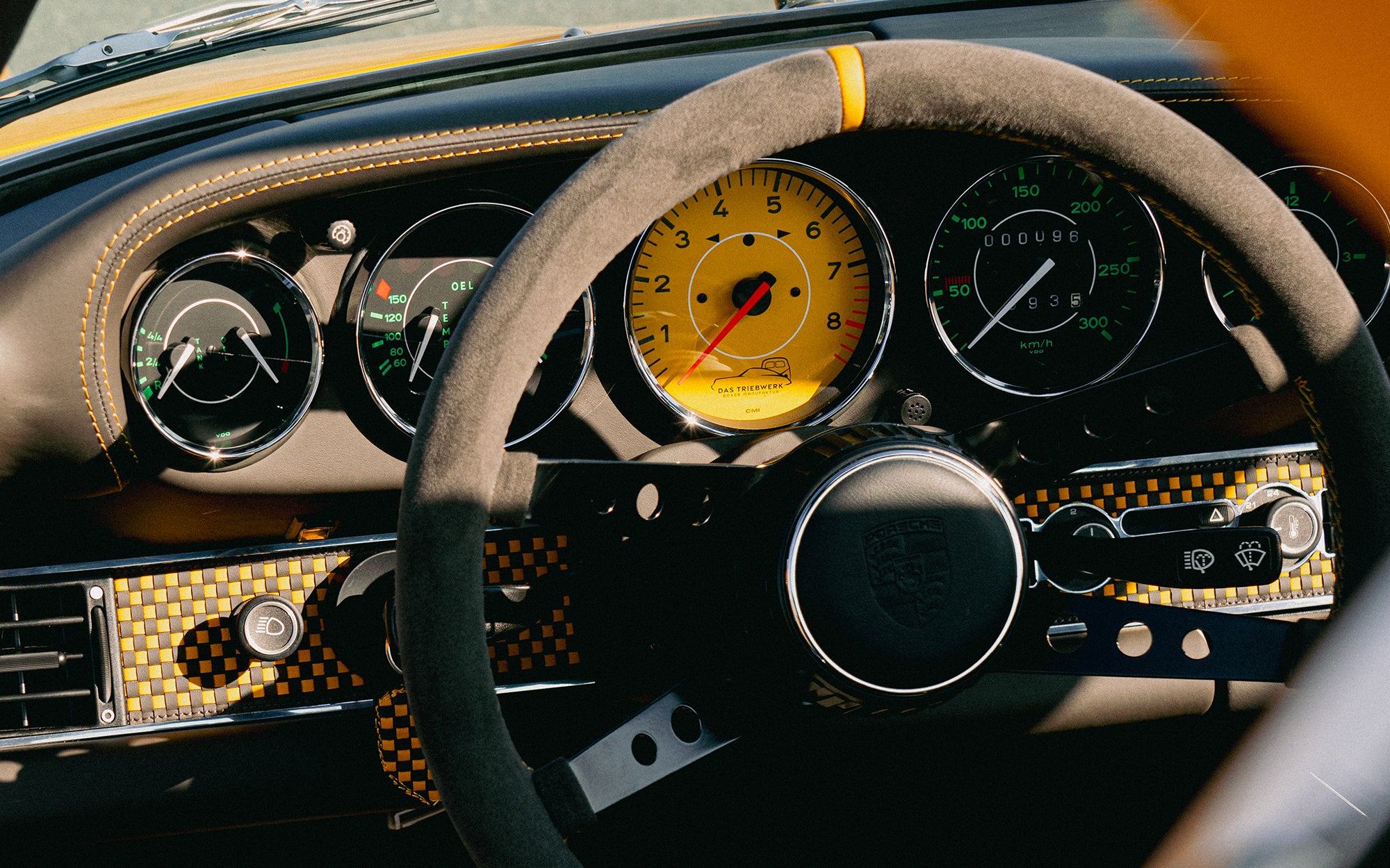Close-up of a Yellow Triebwerk F4.3 Porsche 911 dashboard with steering wheel and gauges.