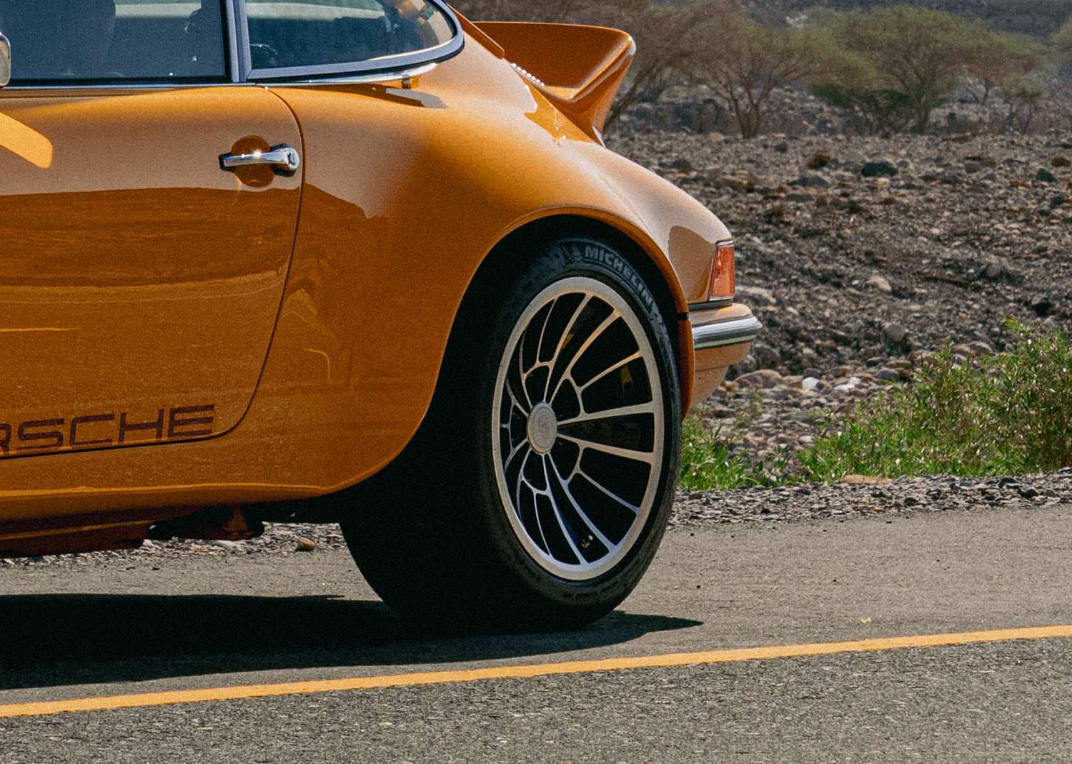 Close-up of a Yellow Triebwerk F4.3 Porsche 911 rear wheel on a road with a desert landscape